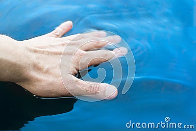Man`s hand touches clean blue water Stock Photo