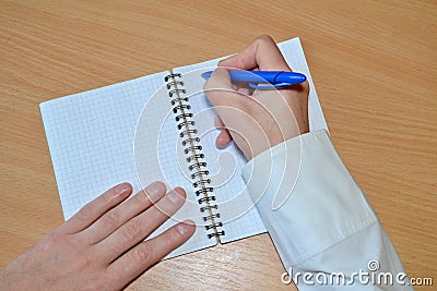 A man`s hand in a white shirt writes the text with a blue pen in a notebook with a spiral on a wooden table, top view Stock Photo