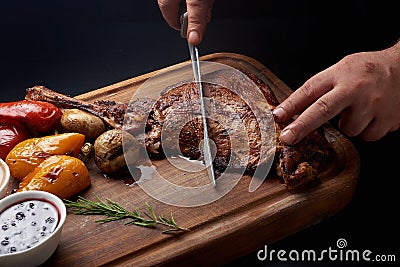 Man`s hands cuts roasted goose legs with grilled belle pepper and mushrooms and souce Stock Photo