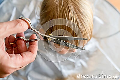 Man`s hands doing toddler haircut with hairdresser scissors at home. Baby boy hair cut diy Stock Photo