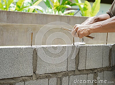 Man`s hands of industrial bricklayer with steel bar installing brick blocks on construction site Stock Photo