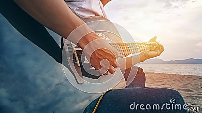 Man`s hands playing acoustic guitar, capture chords by finger on sandy beach at sunset time. playing music concept Stock Photo