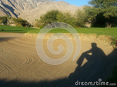 Man's Shadow Appears to be Sitting and watching in Golf Course Sand Trap Stock Photo