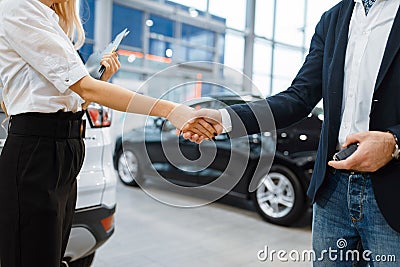 Man and saleswoman shake hands in car dealership Stock Photo