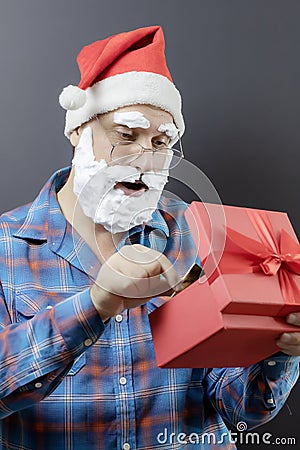 Santa with a white foam beard looks surprised and takes something out of a red gift box Stock Photo