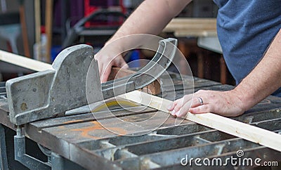 A man sawing through a piece of wood on a table saw. Stock Photo