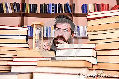 Man, scientist looks at hourglass. Time flow concept. Teacher or student with beard studying in library. Man on serious Stock Photo