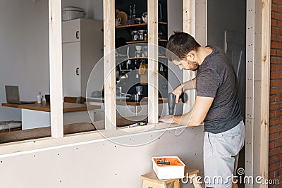 A man with a screwdriver in his hand fixes a wooden frame for a window in his house. Stock Photo