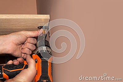 man screws a wooden shelf in a dressing room with a drill. Do-it-yourself home repair and improvement Stock Photo