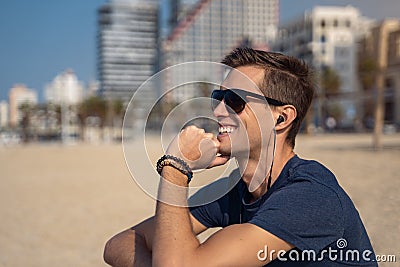 Young man on the beach listening music with headphones. City skyline as background Stock Photo
