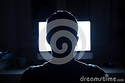 Man seated in front of computer monitor at night Stock Photo