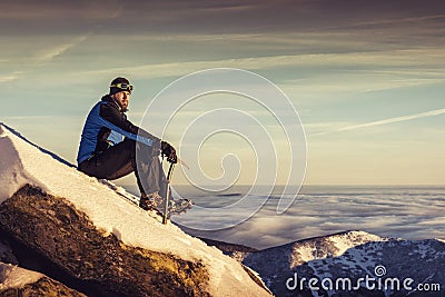 Man seating on top of mountain, male hiker admiring winter scenery on a mountaintop alone with ice ax Stock Photo