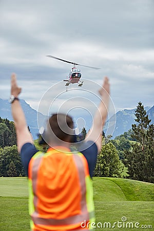 Man seen from behind instructing landing helicopter in the alps Editorial Stock Photo