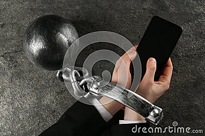 Man shackled with ball and chain holding smartphone at grey table, top view. Internet addiction Stock Photo