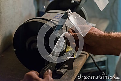 Man sharpens a knife on an electric grindstone Stock Photo