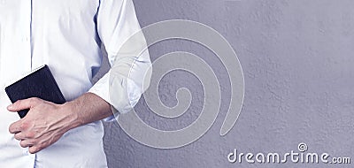 A man in a shirt holds a Bible book in his hands. On a gray background. Pastor. Prayer. Stock Photo