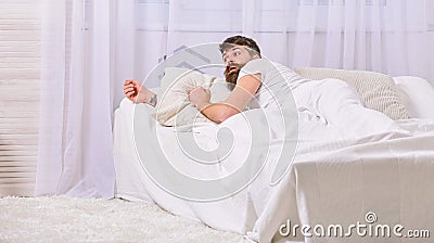 Man in shirt laying on bed awake, white curtain on background. Wake up and oversleep concept. Macho with beard and Stock Photo