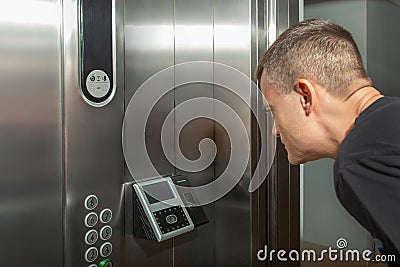 A man shows his face to a fingerprint access control terminal with a facial recognition function installed in the elevator Stock Photo