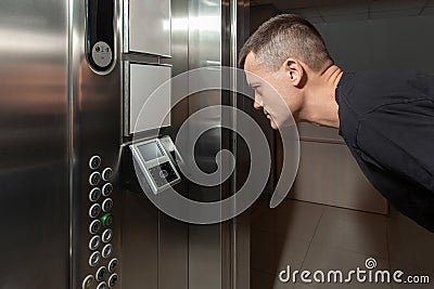 A man shows his face to a fingerprint access control terminal with a facial recognition function installed in the elevator Stock Photo