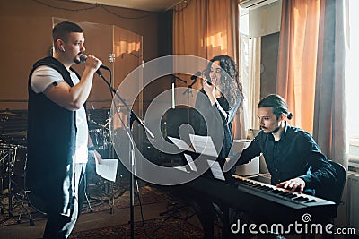 Man sings into microphone to accompaniment of electronic keyboards and teacher shows shape of mouth in vocal lesson Stock Photo