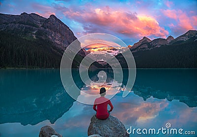 Man sit on rock watching Lake Louise morning clouds with reflect Stock Photo