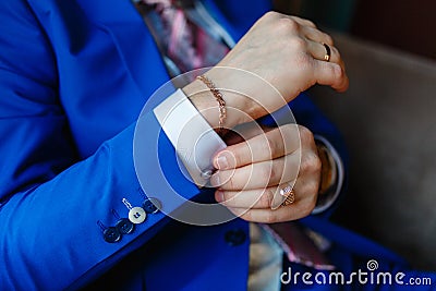 The man sits in an armchair and fixes the cuffs on a white shirt and a stylish blue jacket with expensive gold accessories, watche Stock Photo