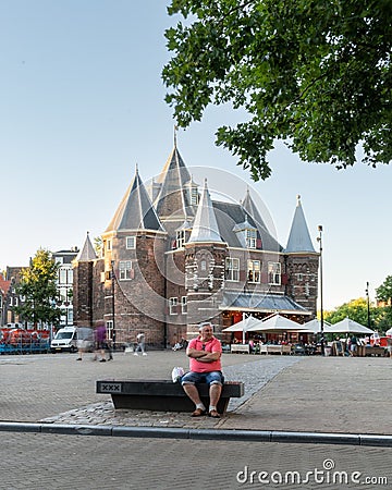 A man sits on a bench outside The Waag restaurant and cafe in Nieuwmarkt. Editorial Stock Photo