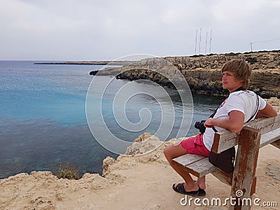 A man sits on a bench on a rock, overlooking the sea. Cyprus, Protaras, May 2018. Stock Photo