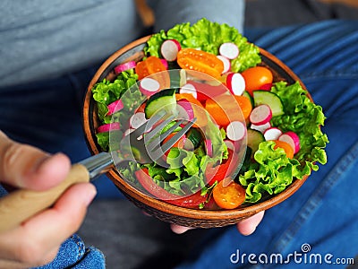 A man sits on the floor and eats a delicious green salad with orange tomatoes, radishes and cucumber Stock Photo