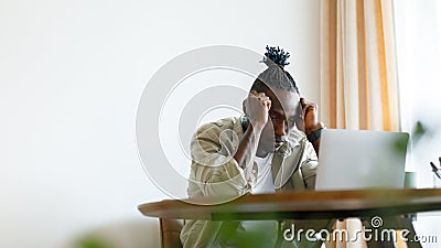 A man sits at home in a tense mood and looks at a laptop. The man looks flustered, with hands touching his head. Stock Photo