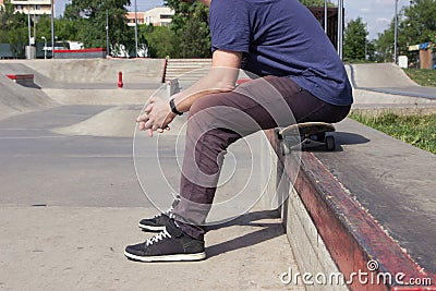 A man sits on a skateboard on the background of a skatepark. Feet close up. lifestile concept. Stock Photo