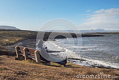 Man sitting on a bench with a beautiful view on Atlantic ocean and looking on the screen of his smart phone, Stock Photo
