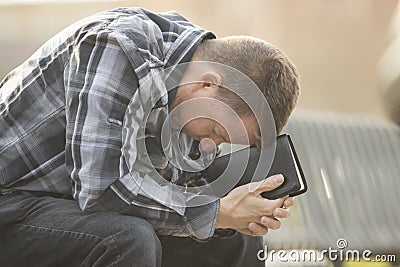 Man sitting on bench and praying with Bible Stock Photo