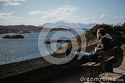Man sitting on a bench, relaxing in the sun in Kyle of Lochalsh, Scotland. Stock Photo