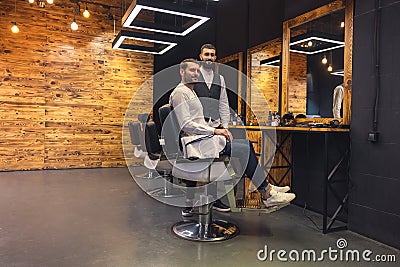 Man sitting on chair in barbershop with his master hairdresser. Stock Photo
