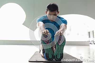 Man sitting down on exercise mat while touching his toes during stretching Stock Photo