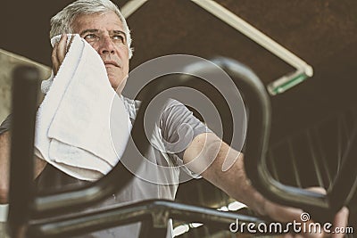 Man sitting on exercise machine. Man wipes his face with Stock Photo