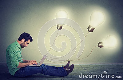 man sitting on floor using a laptop with many light bulbs plugged in it Stock Photo