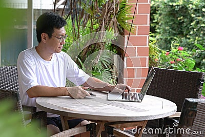 Man sitting at his house patio with garden view, working on his laptop. Work from home concept Stock Photo