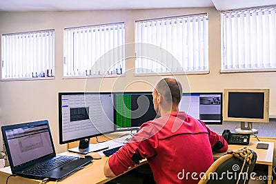 A man is sitting at the office behind a worker`s desk. The engineer monitors the computer network. A specialist works for several Stock Photo