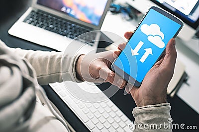 Man sitting at office desk using cloud service on smartphone for data transfer and synchronization Stock Photo