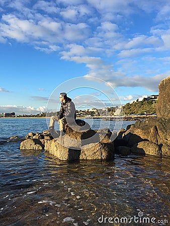 Man sitting on rocks on beach Stock Photo