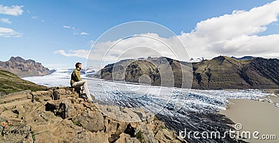 Man sitting on rocks overlooking Skaftafellsjokull part of Vatnajokull glacier in Skaftafell national park, Iceland Stock Photo