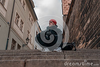 Man Sitting on Stairs in Old European City And Holding Photo Camera. Contemporary Stylish Blogger And Photographer Stock Photo