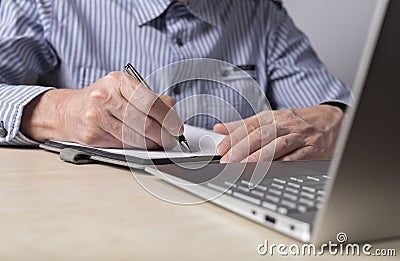 Man sitting at table with laptop and writing with pen in diary. Hands closeup. Taking online courses, preparation for Stock Photo
