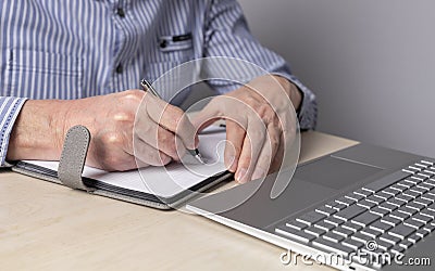 Man sitting at table with laptop and writing with pen in notebook. Hands closeup. Student or freelancer lifestyle. Using Stock Photo