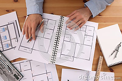 Man with sketchbook of construction drawings and pencil at wooden table, top view Stock Photo