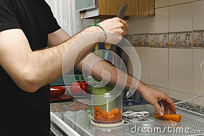 Man slicing carrots to put them in the mixing machine in the kitchen Stock Photo