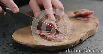 Man slicing fuet sausage on olive wood board Stock Photo