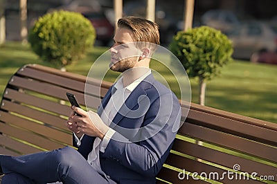 Man with smartphone in park. Manager with mobile phone on sunny outdoor. Businessman in blue suit relax on bench Stock Photo